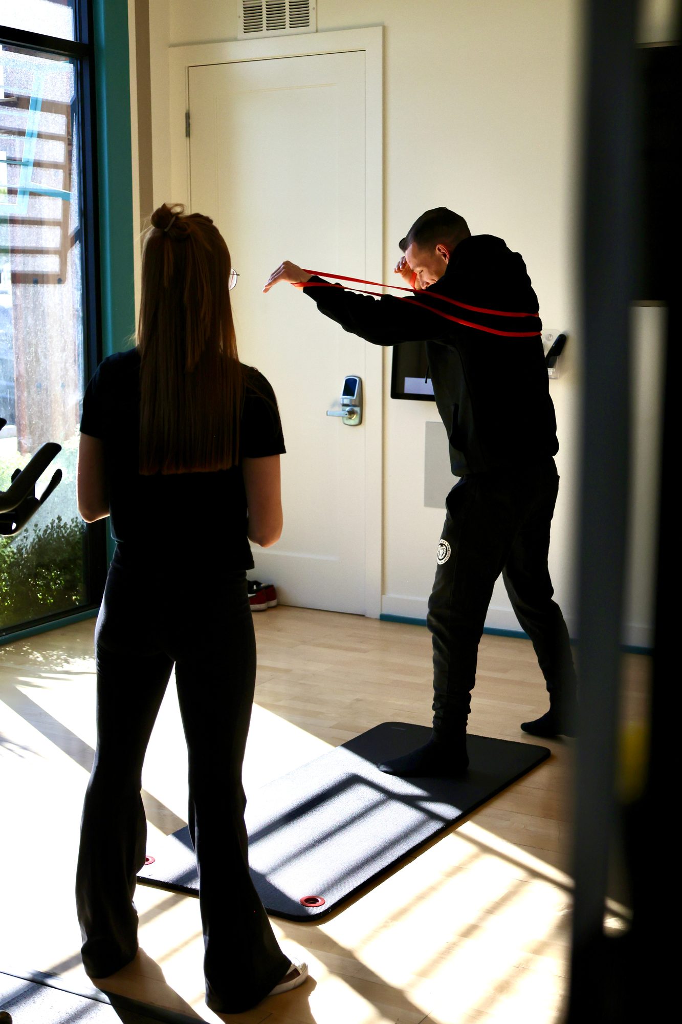 Coach Ilona watching an athlete work his shoulders through a resistance-band pull at the studio