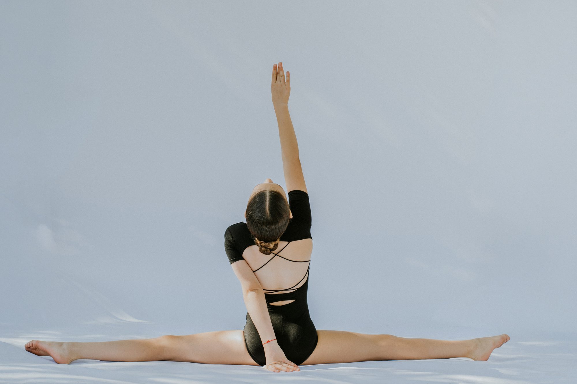 A young gymnast holding a full split with one arm raised, seen from behind