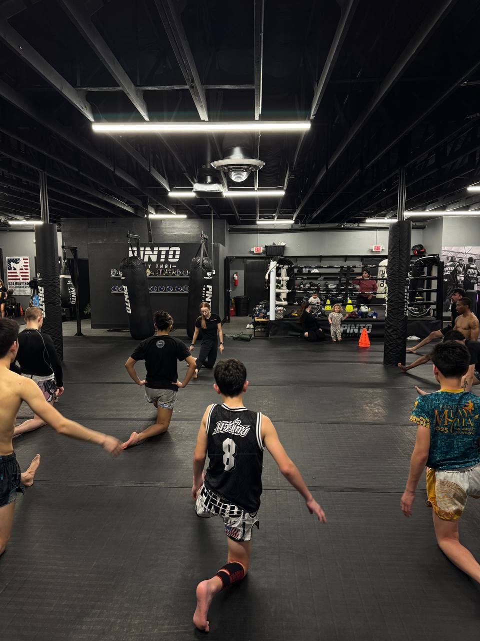 Fighters stretching on the mats of a combat-sports gym during a team session